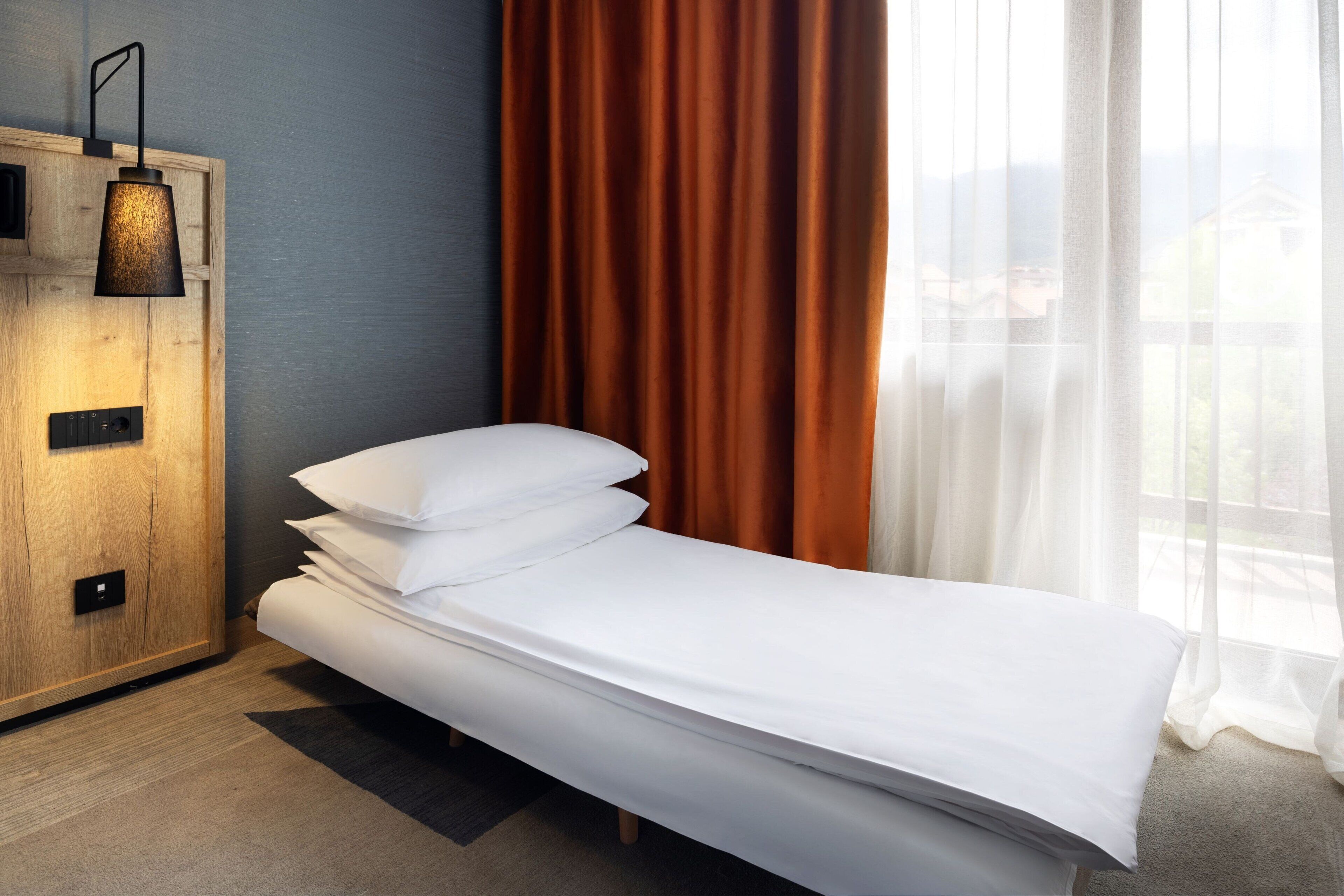 A single bed with white bedding in a room with a wooden cabinet and a wall-mounted lamp.