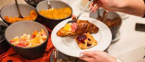 A breakfast setting with bowls of cereal and fruits, a croissant, and a pot of grains.