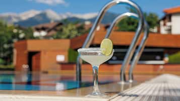 A clear view of a poolside bar with a margarita glass on the edge, a metal pool ladder, and a mountainous backdrop.