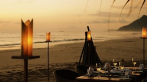 A beachside dining setup with tables and chairs, candles, and a view of the ocean. - Amara Ocean Resort (Thandwe)