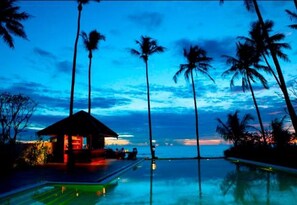 A resort with a pool, palm trees, and a building with lights. - Amara Ocean Resort (Thandwe)