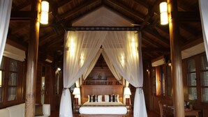 A spacious bedroom with a large bed, wooden headboard, and a canopy. There are two bedside tables with lamps and a wooden bench at the foot of the bed. - Amara Ocean Resort (Thandwe)