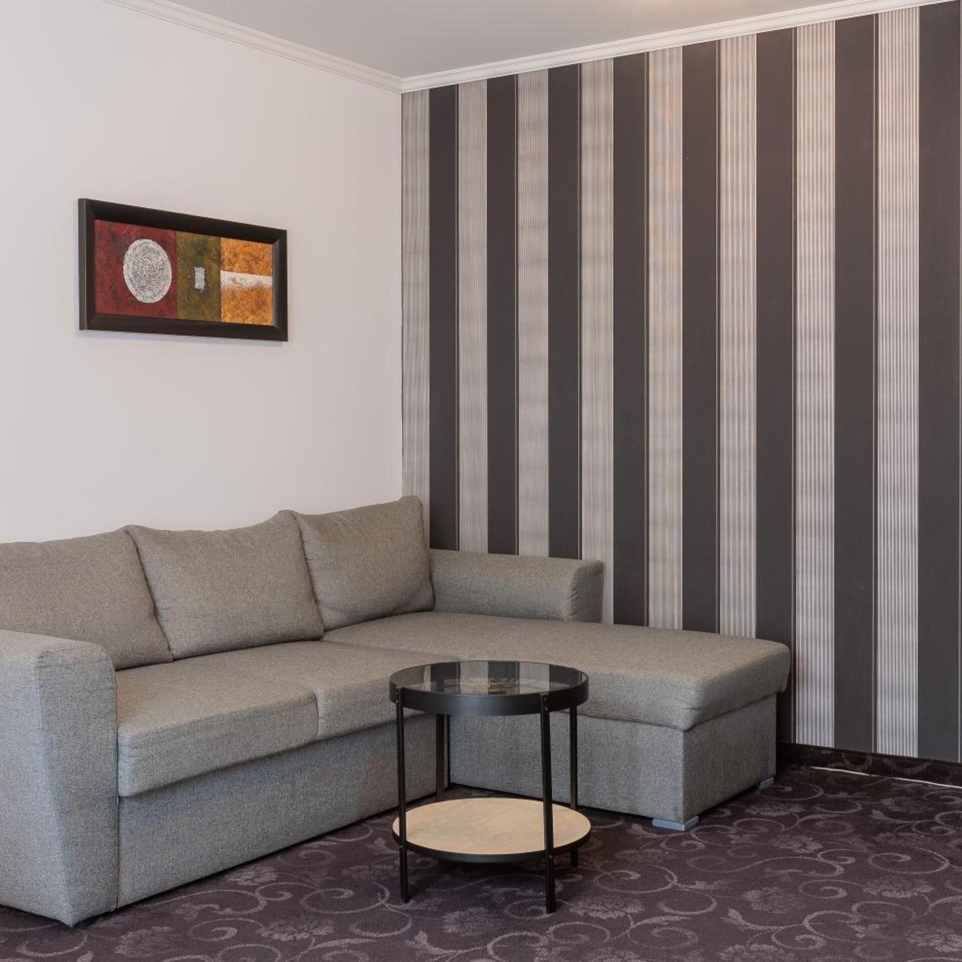 A corner room with a gray sofa, a small round table, and a striped wallpaper.