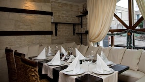 Un comedor con mesas dispuestas para cuatro, una pared de piedra y una ventana con cortinas.
