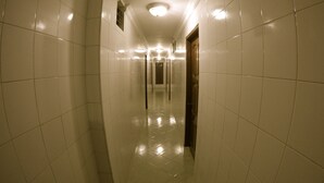 Un long couloir étroit aux murs recouverts de carreaux blancs et au sol brillant, qui mène à une porte au fond.