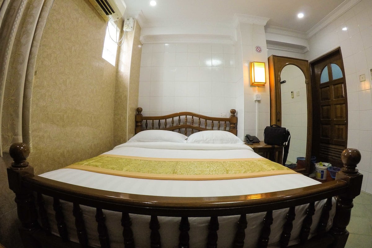 A hotel room with a wooden bed, a bedside table, a mirror, and a door.
