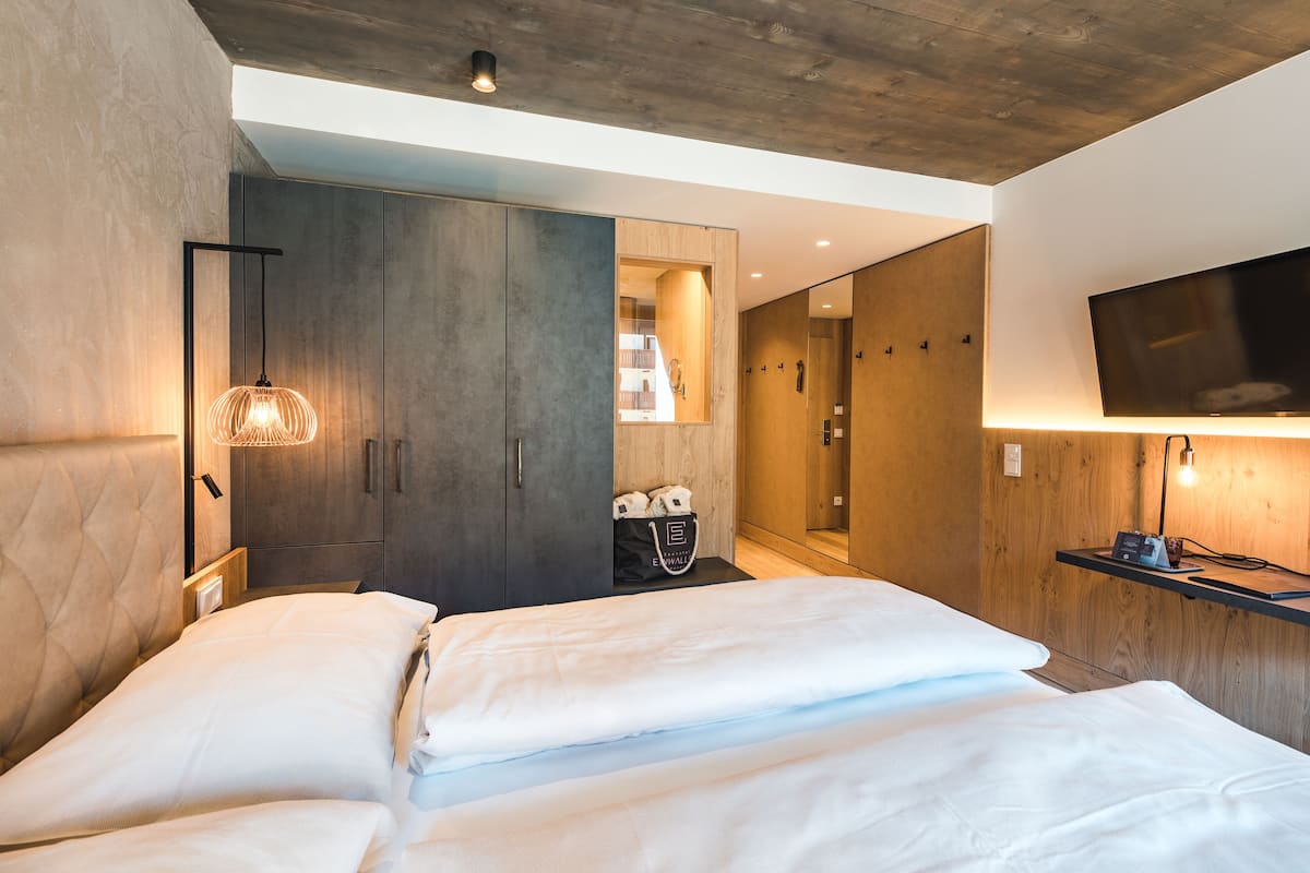 Una habitación de hotel moderna con una cama grande, un armario, un espejo, un televisor y un escritorio con una lámpara.