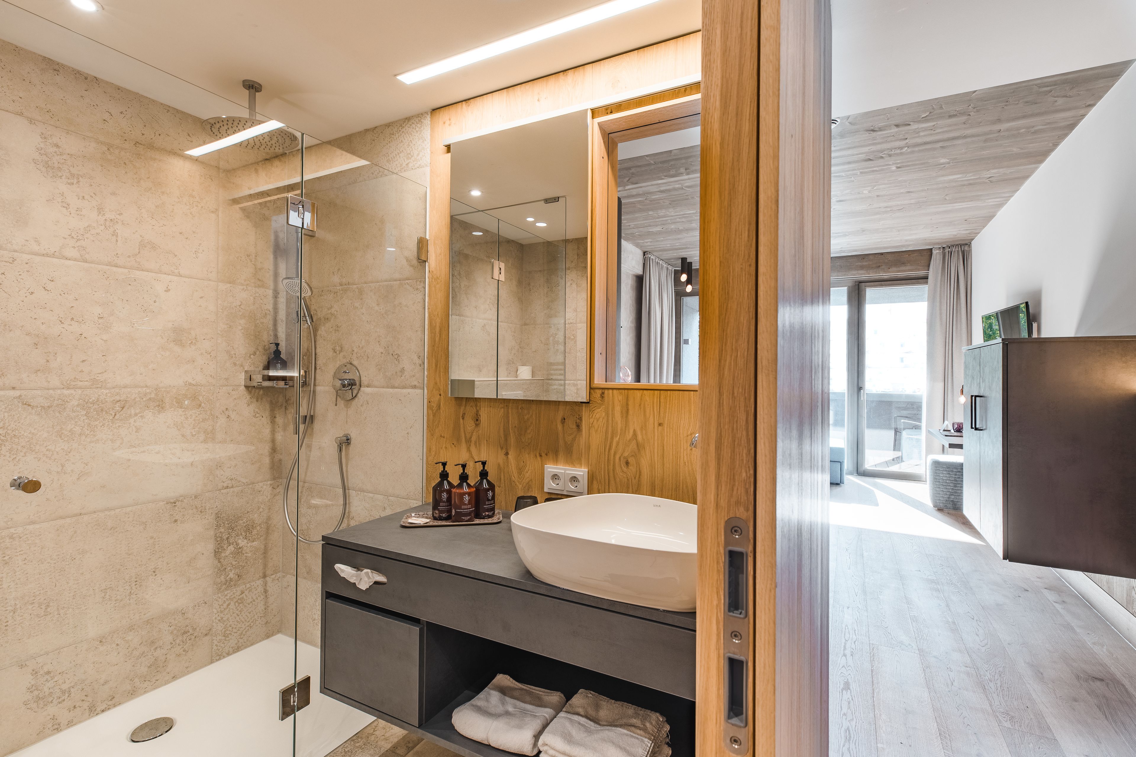 A modern bathroom with a glass-enclosed shower, a large mirror, and a wooden vanity.