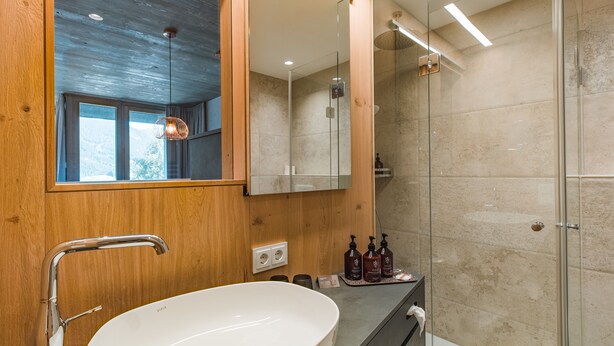 Een moderne badkamer met een grote witte wasbak, houten lambrisering, een douchecabine van glas en een grote spiegel.
