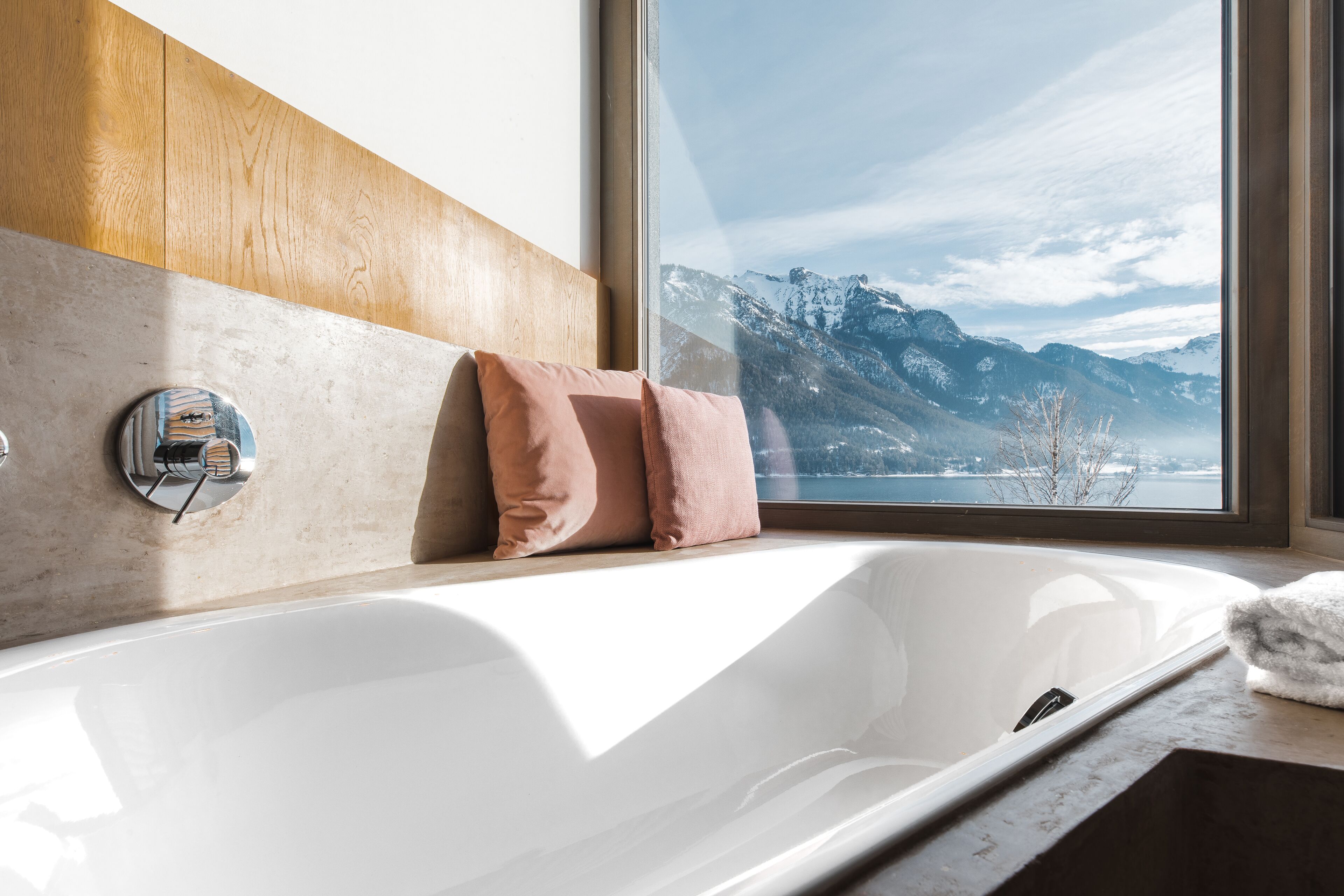 A bathroom with a bathtub, wooden paneling, and a window with a mountain view.