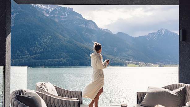 Ein Zimmer mit Blick auf einen See und Berge, ausgestattet mit einer Couch und einem Tisch mit einem Buch und einer Tasse.