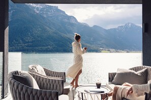Habitación con vistas a un lago y montañas, que incluye un sofá y una mesa con un libro y una taza.
