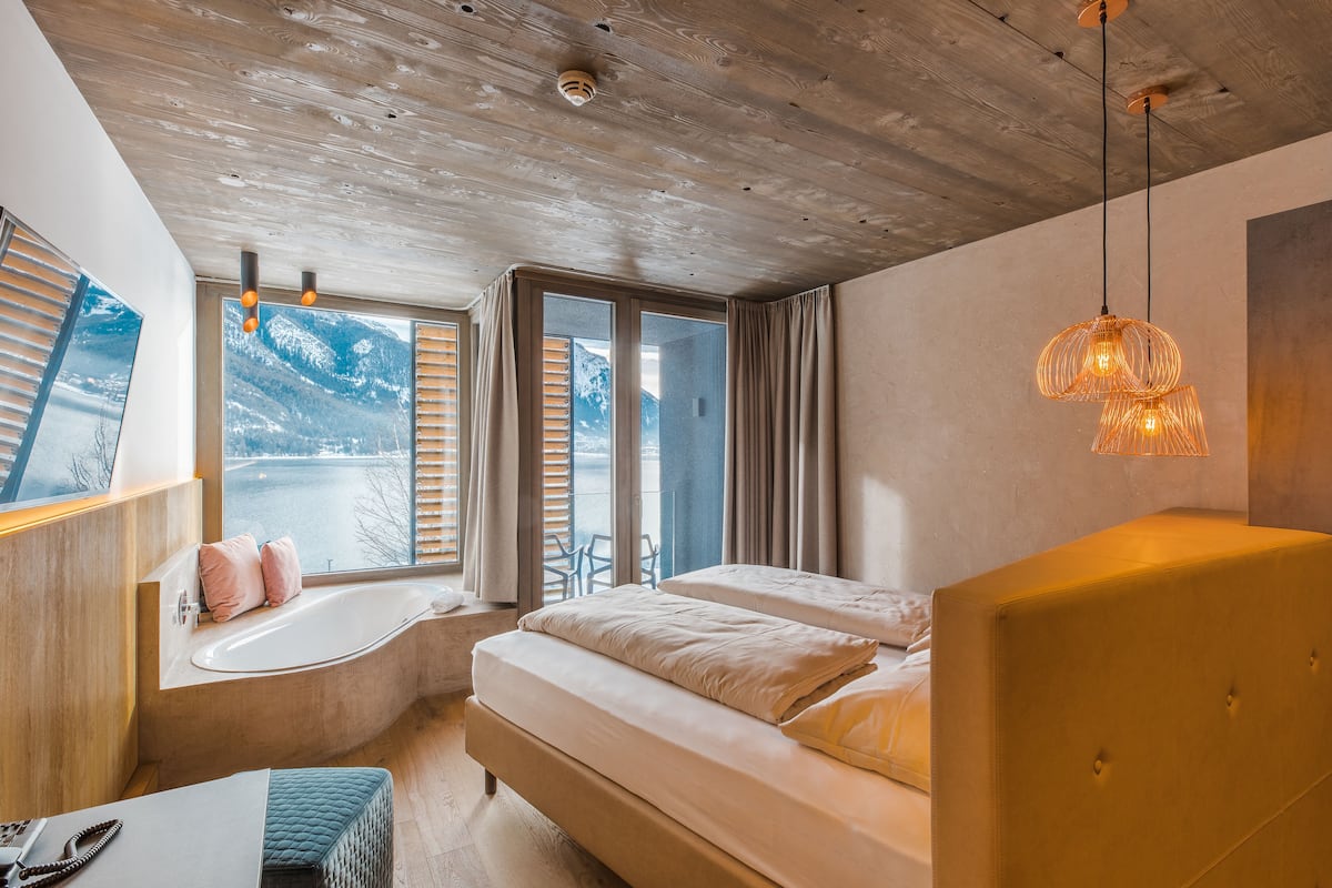 Un dormitorio moderno con un ventanal grande, una bañera y una cama con cabecero.