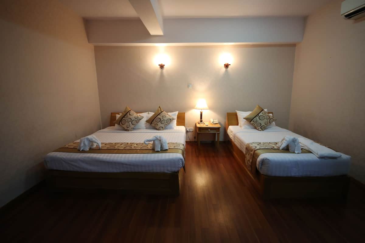A hotel room with two beds, wooden flooring, a nightstand with a lamp, and wall-mounted lights.