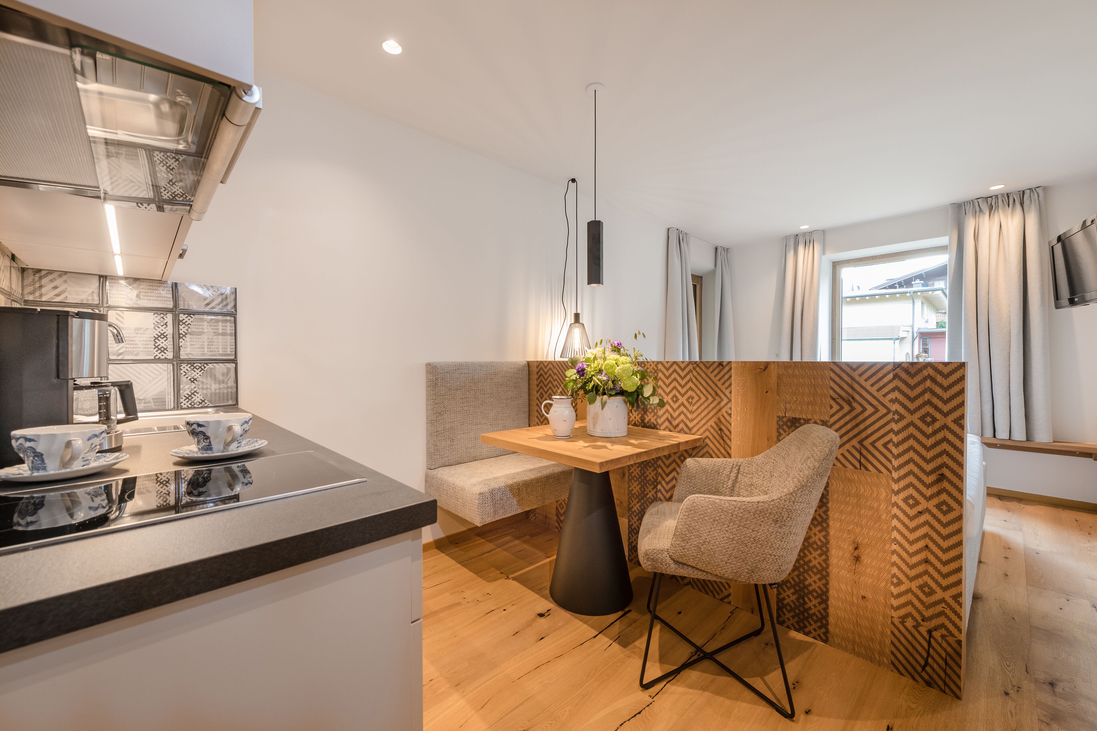 Una cocina compacta con estufa moderna, un comedor con mesa de madera y una silla, y un pared con diseño.