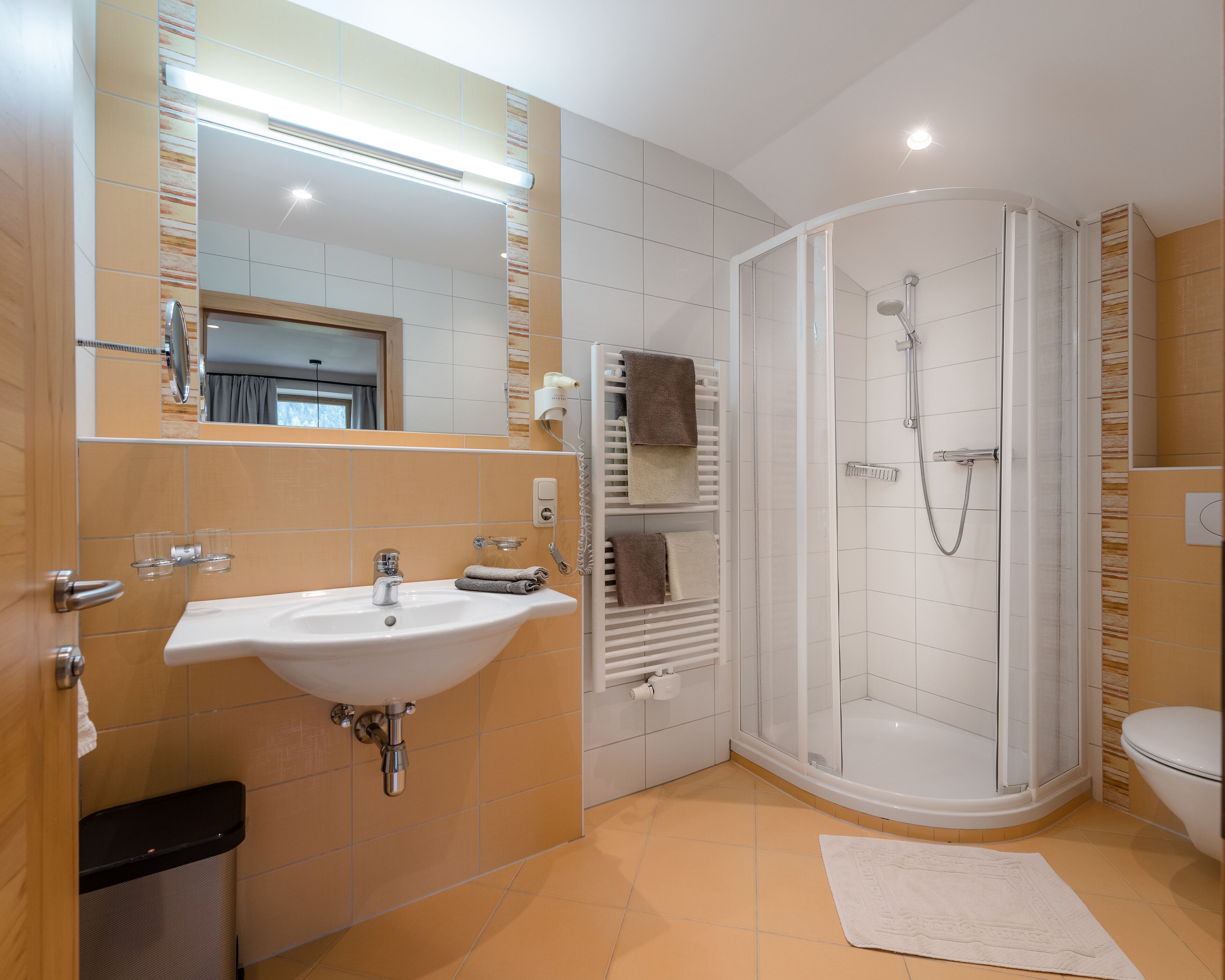 A modern bathroom with a white sink, a glass-enclosed shower, and a toilet.