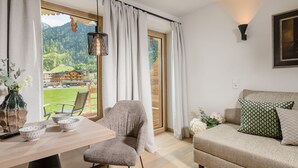 Una camera moderna con un tavolo di legno, due sedie, un divano e vista su un paesaggio montano.