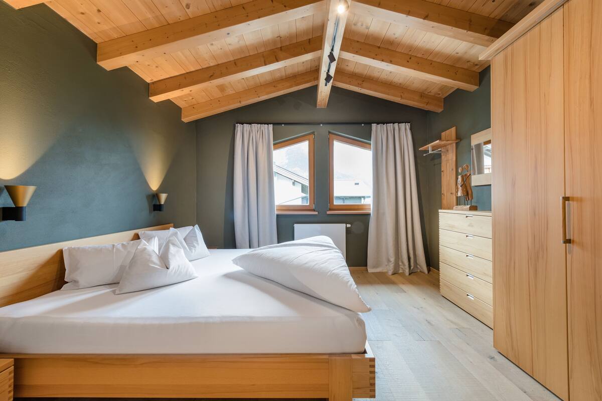 Une chambre à coucher avec un lit en bois, une commode et une fenêtre avec des rideaux.