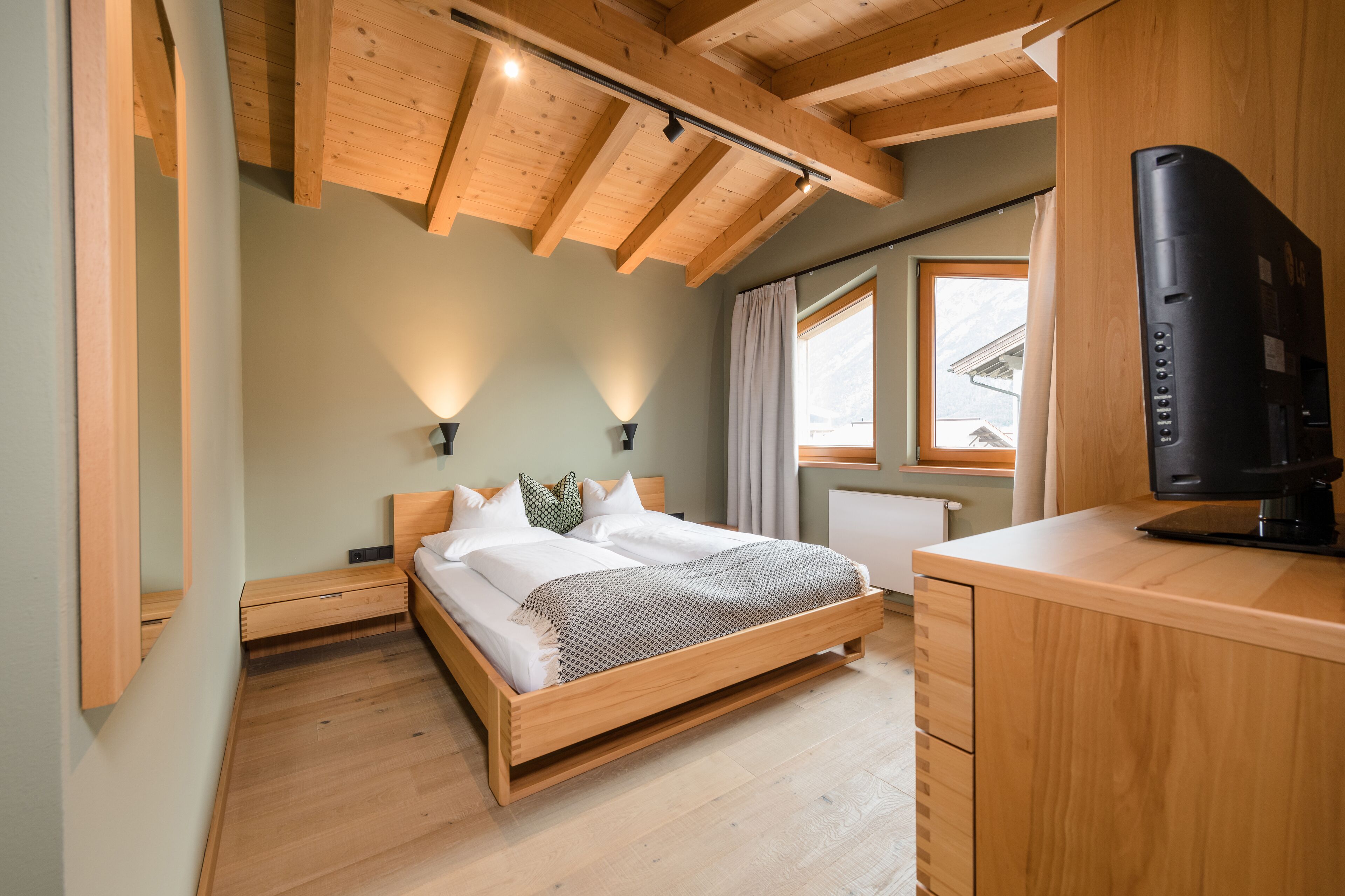 A bedroom with a wooden bed, bedside tables, a desk, and a TV.