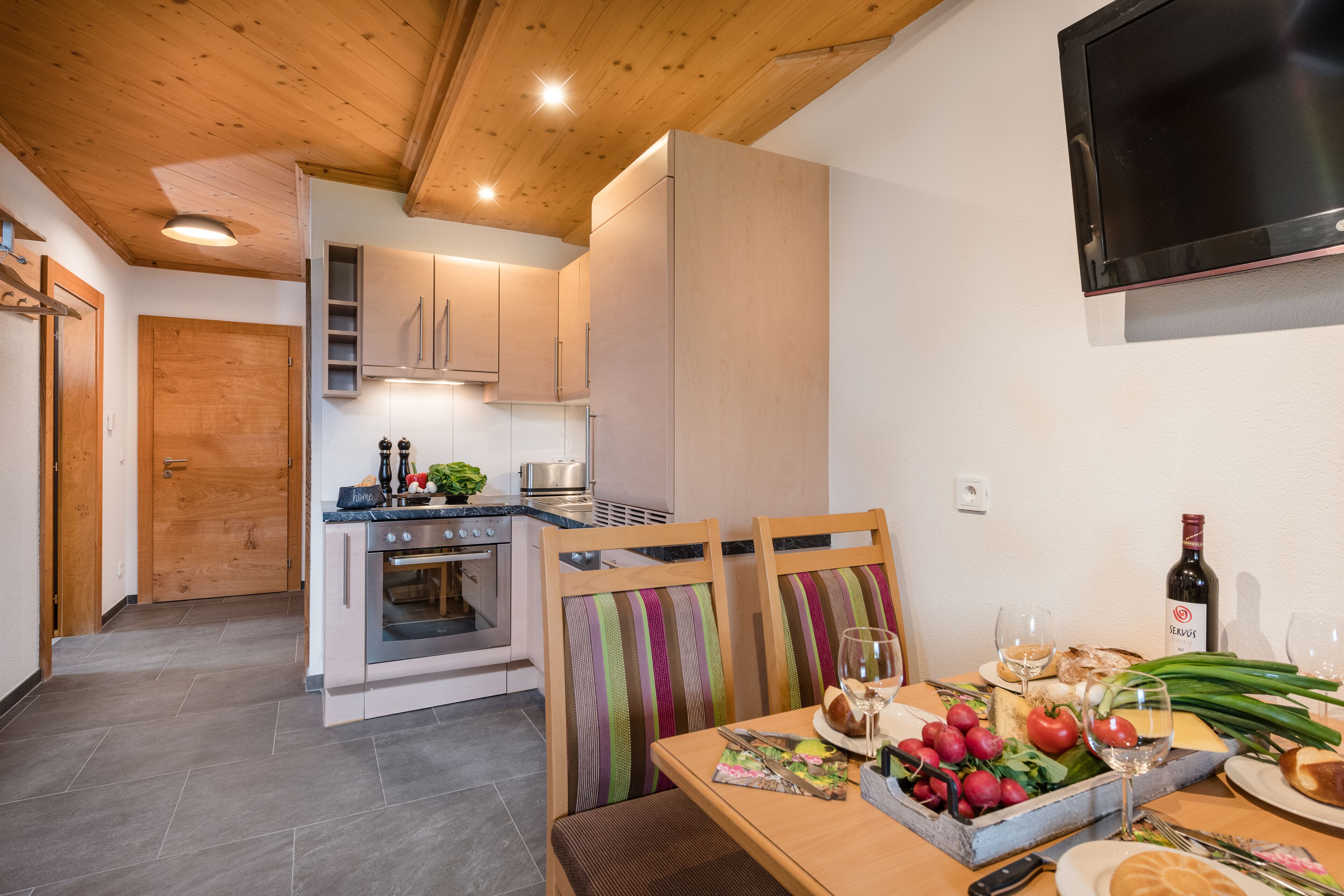 Een moderne keuken met houten kastjes, een inbouwoven en een eethoek met een tafel gedekt voor twee personen.
