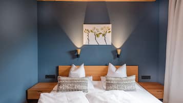 Ein Hotelzimmer mit einem hölzernen Kopfende, zwei Nachttischen, einem Bett mit weißen Leinen, dekorativen Kissen und einem an der Wand hängenden Blumenbild.