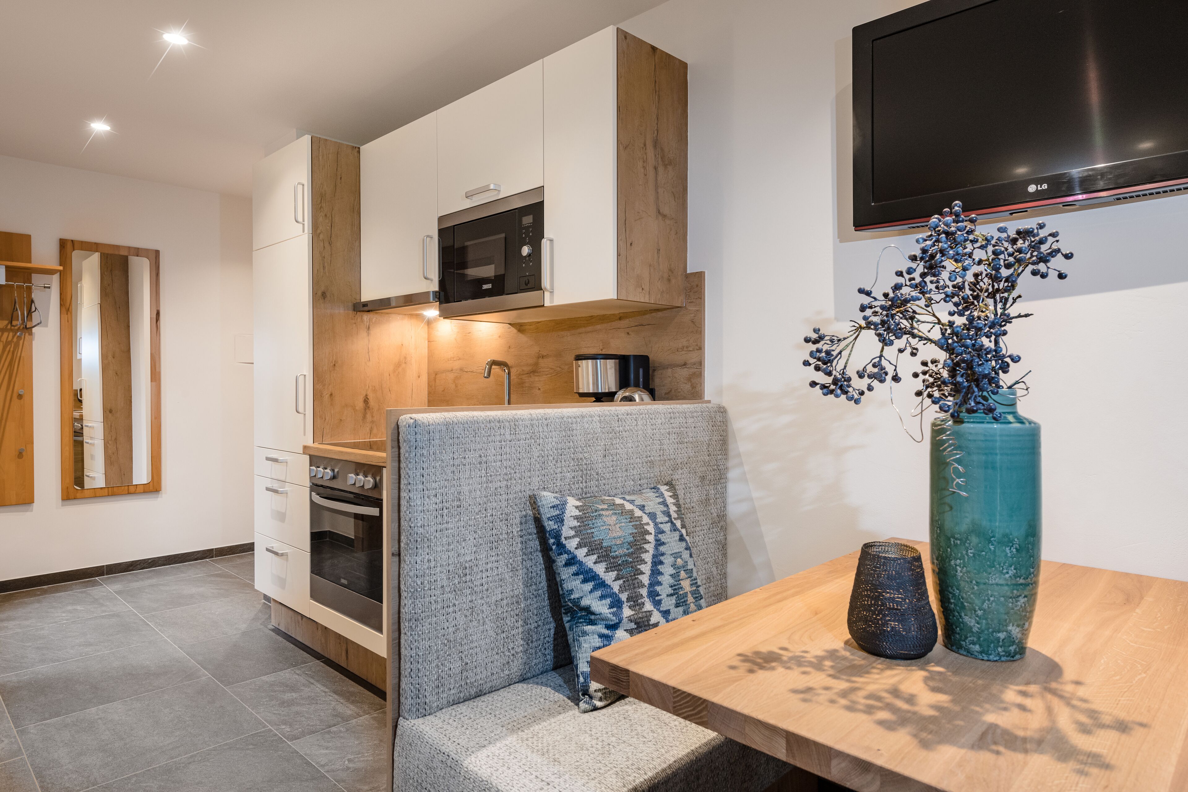 Una cocina moderna con electrodomésticos integrados, un revestimiento de madera y una zona de comedor con mesa y objetos decorativos.