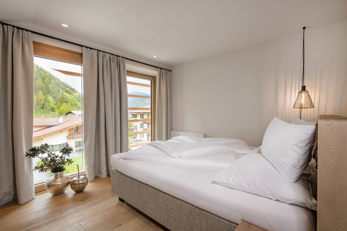 Une chambre avec un grand lit, une vue sur un paysage montagneux et une fenêtre avec des rideaux.