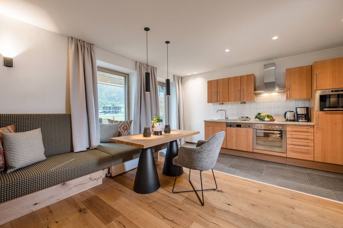 Une cuisine moderne avec des meubles en bois, un four encastré et un coin repas comprenant une table et des chaises en bois.