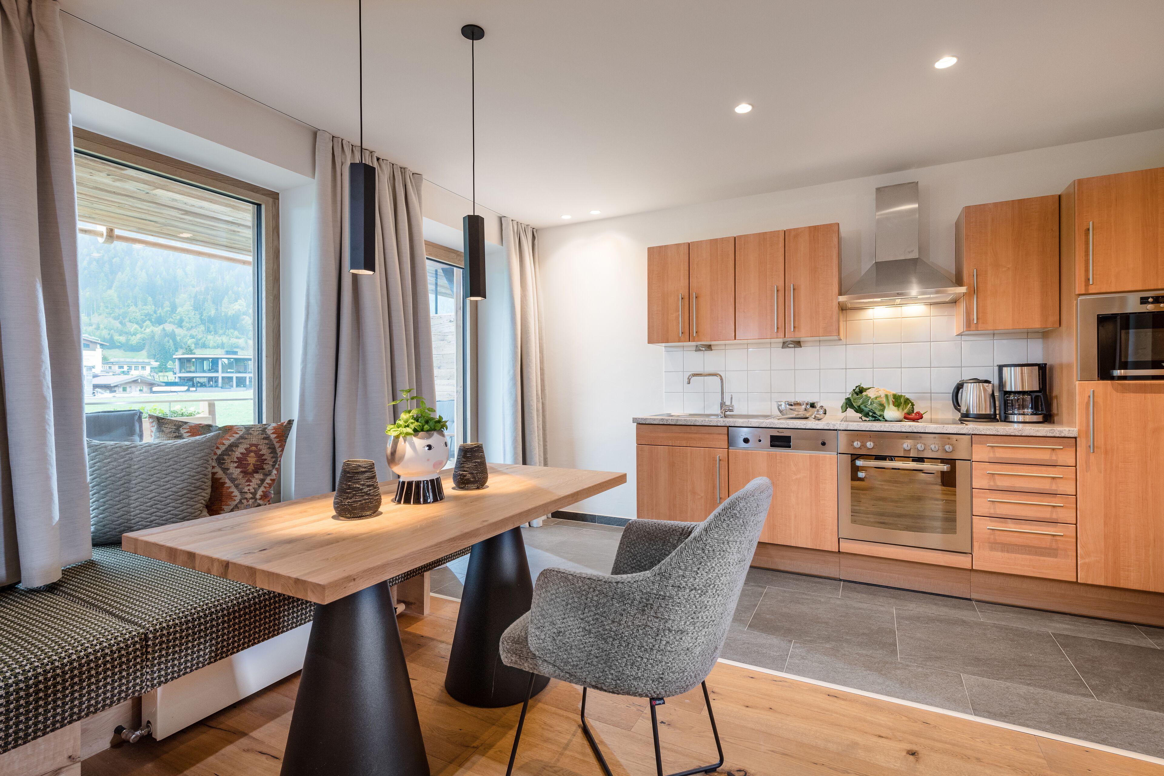 A modern kitchen with wooden cabinets, a built-in oven, and a dining area with a bench and table.