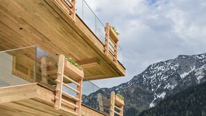 Un balcone in legno con ringhiere in vetro che si affaccia su un paesaggio montuoso.
