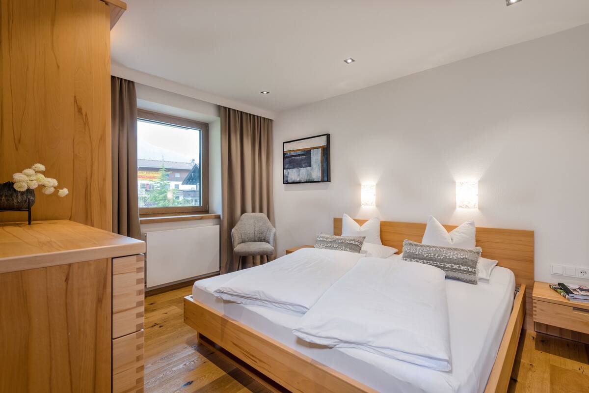 Une chambre d’hôtel moderne avec un lit en bois, un bureau, une chaise et une fenêtre avec des rideaux.