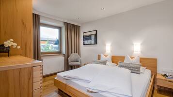 A modern hotel room with a wooden bed, a desk, a chair, and a window with curtains.