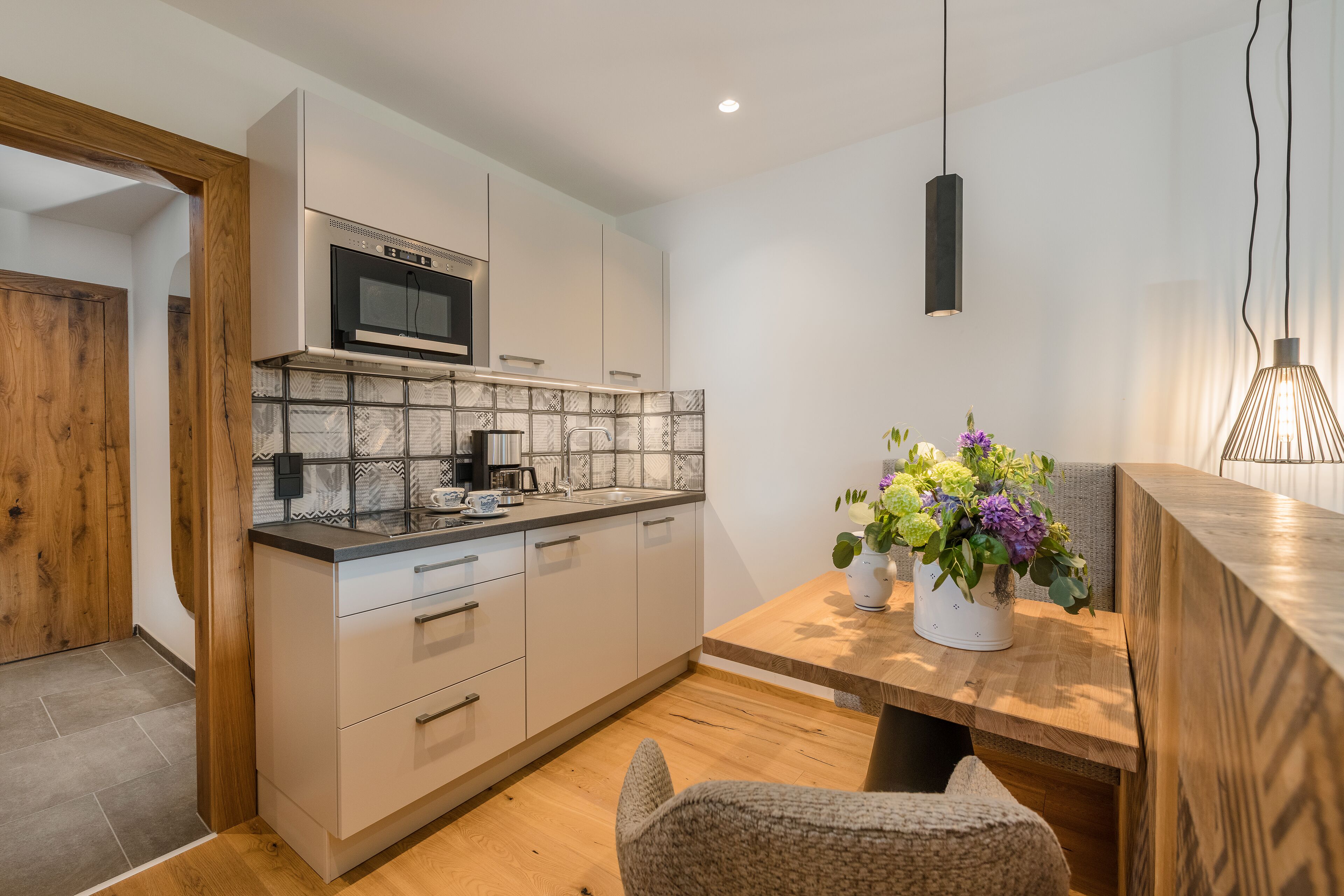 Una cocina moderna con microondas, estufa y lavamanos. Hay una mesa de comedor de madera con un florero.