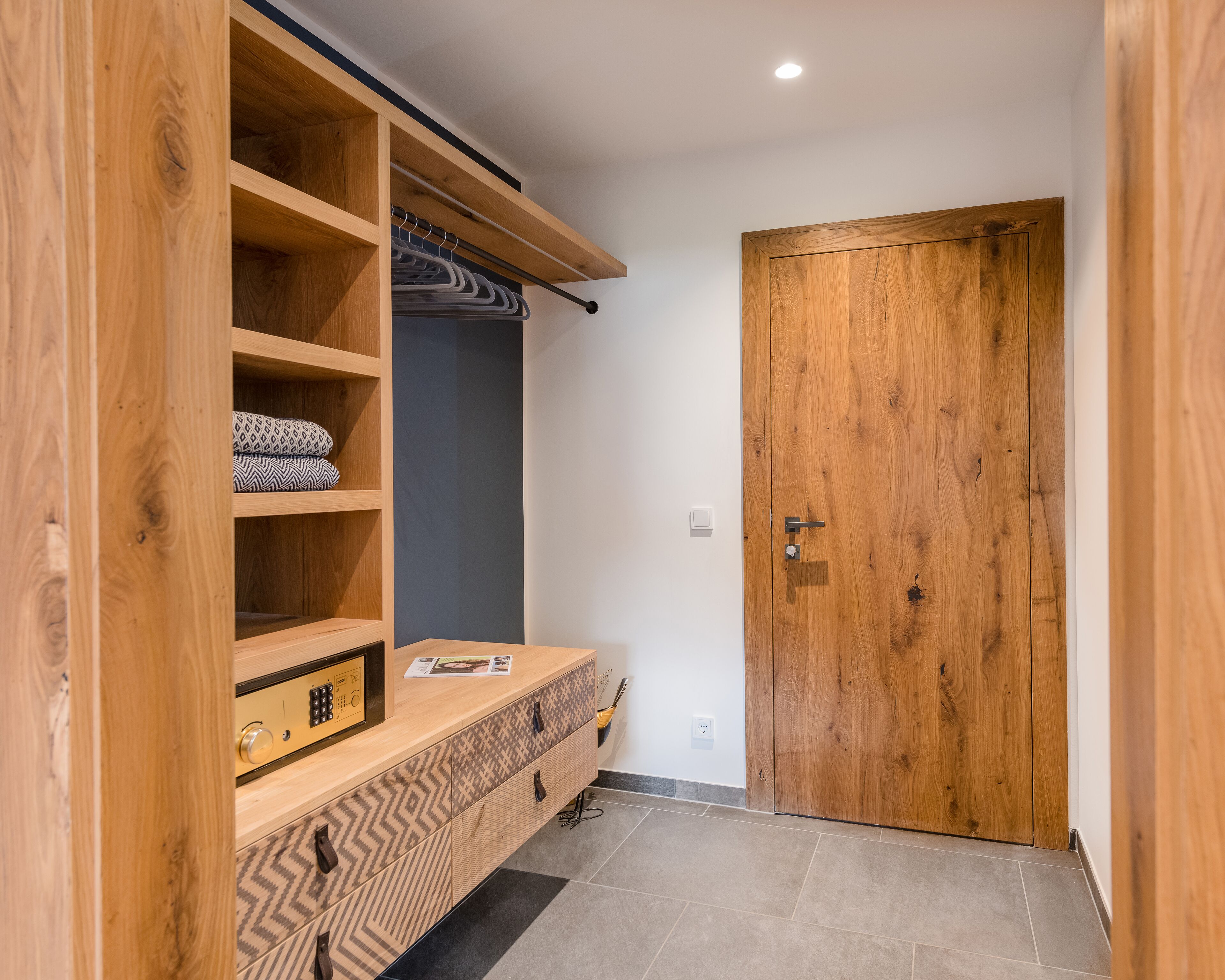 Un armario de madera con múltiples estantes y un banco integrado, una puerta de madera y piso de baldosas.