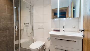 Un baño moderno con cabina de ducha de vidrio, inodoro blanco, tocador con espejo y un cubo de basura.