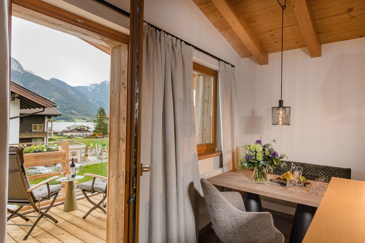 Un balcon avec un plancher en bois, une table avec des chaises, un luminaire suspendu et une vue sur les montagnes.