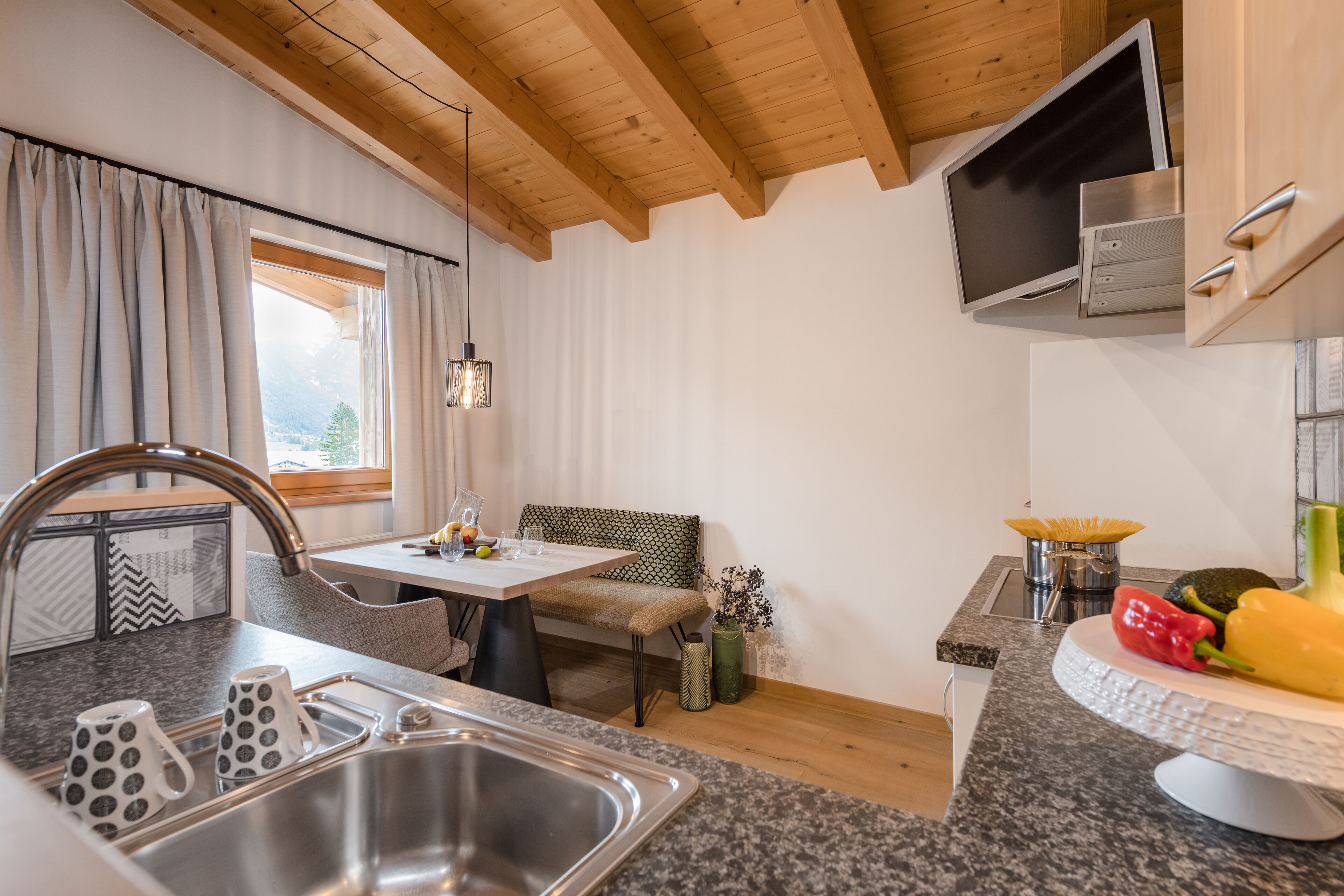 A modern kitchen with a granite countertop, stainless steel sink, and wooden ceiling beams.