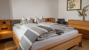 Una cama bien hecha con ropa de cama estampada, una mesita de noche con lámpara, un aparador de madera y un cuadro colgado en la pared.