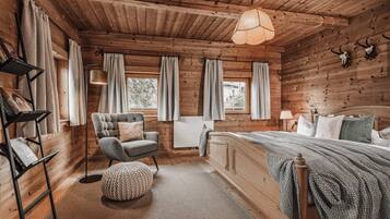Acogedor dormitorio de cabaña de madera con cama, una silla, un atril y una ventana con cortinas.