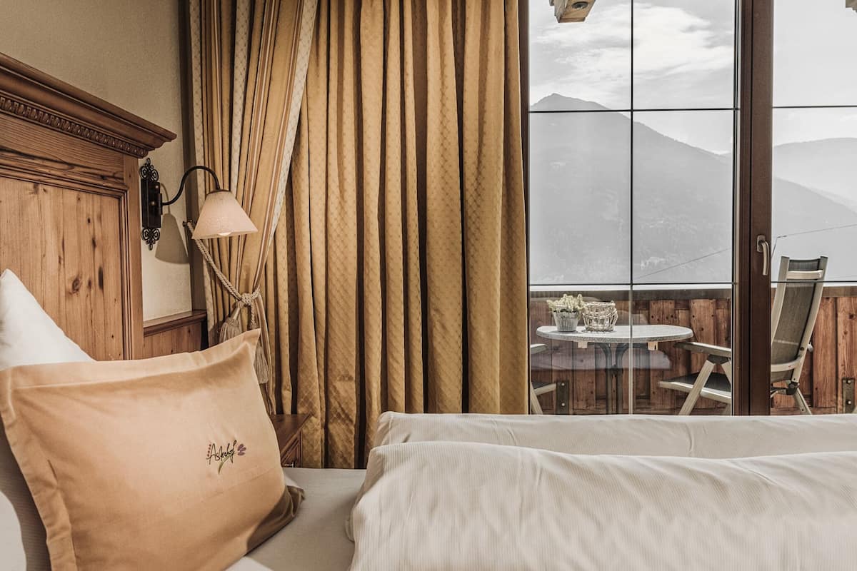 Une chambre d’hôtel avec un lit, une tête de lit en bois, une fenêtre avec des rideaux et une vue sur les montagnes.
