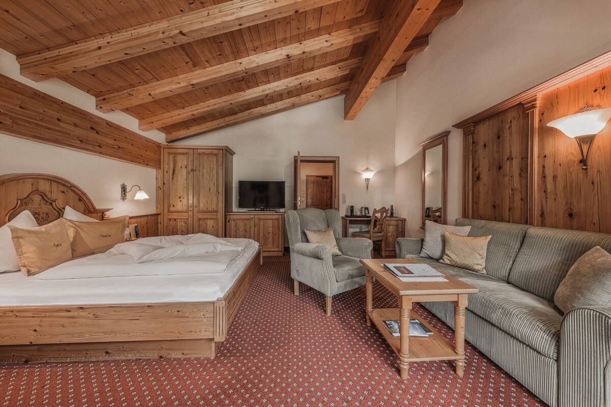 Une chambre avec un plafond en bois, un lit, un canapé, une chaise, une table et un téléviseur.