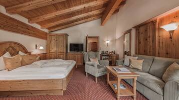 A bedroom with a wooden ceiling, a bed, a sofa, a chair, a table, and a TV.