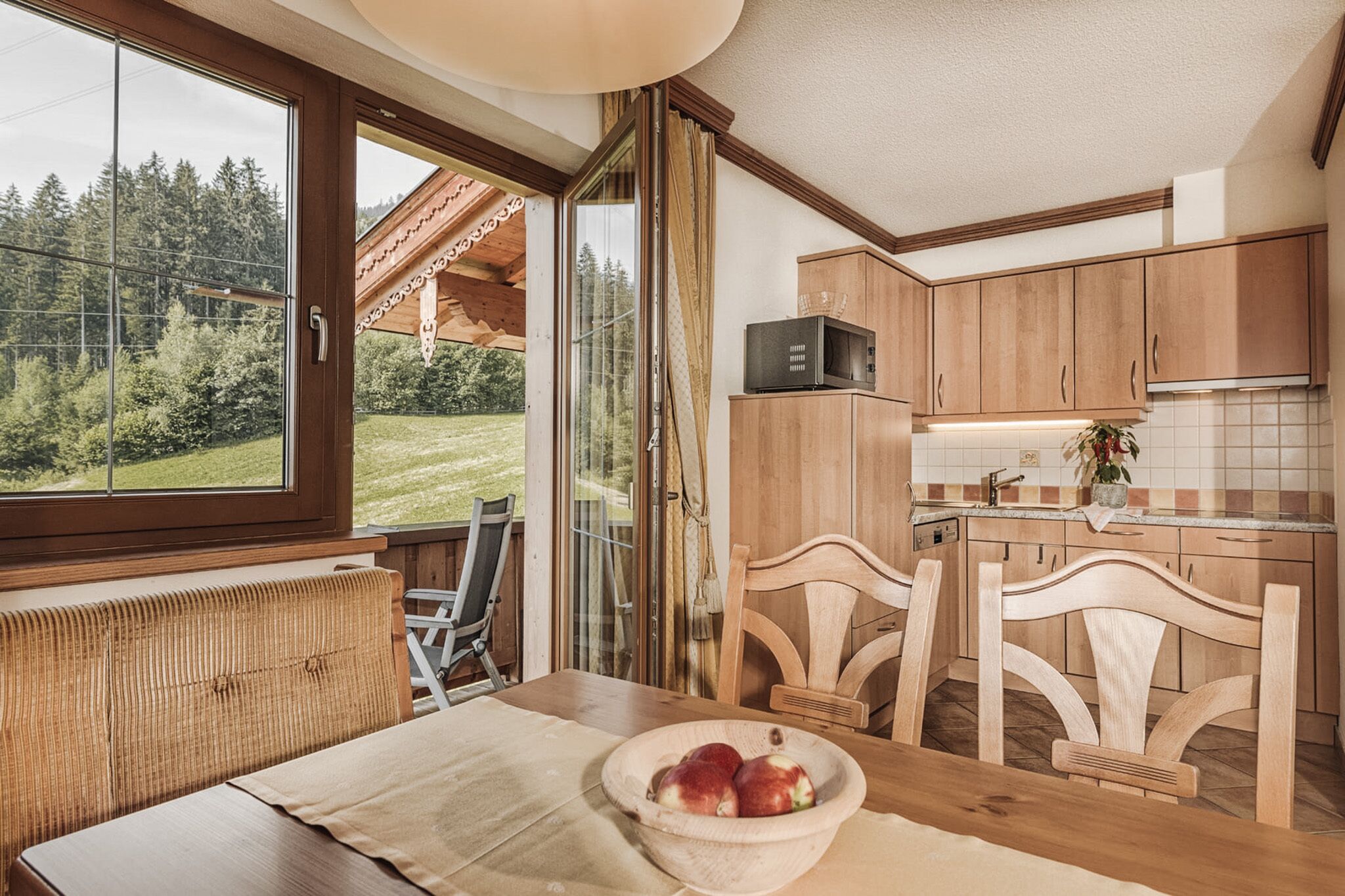 Una cocina con armarios de madera, microondas y comedor con mesa y sillas.