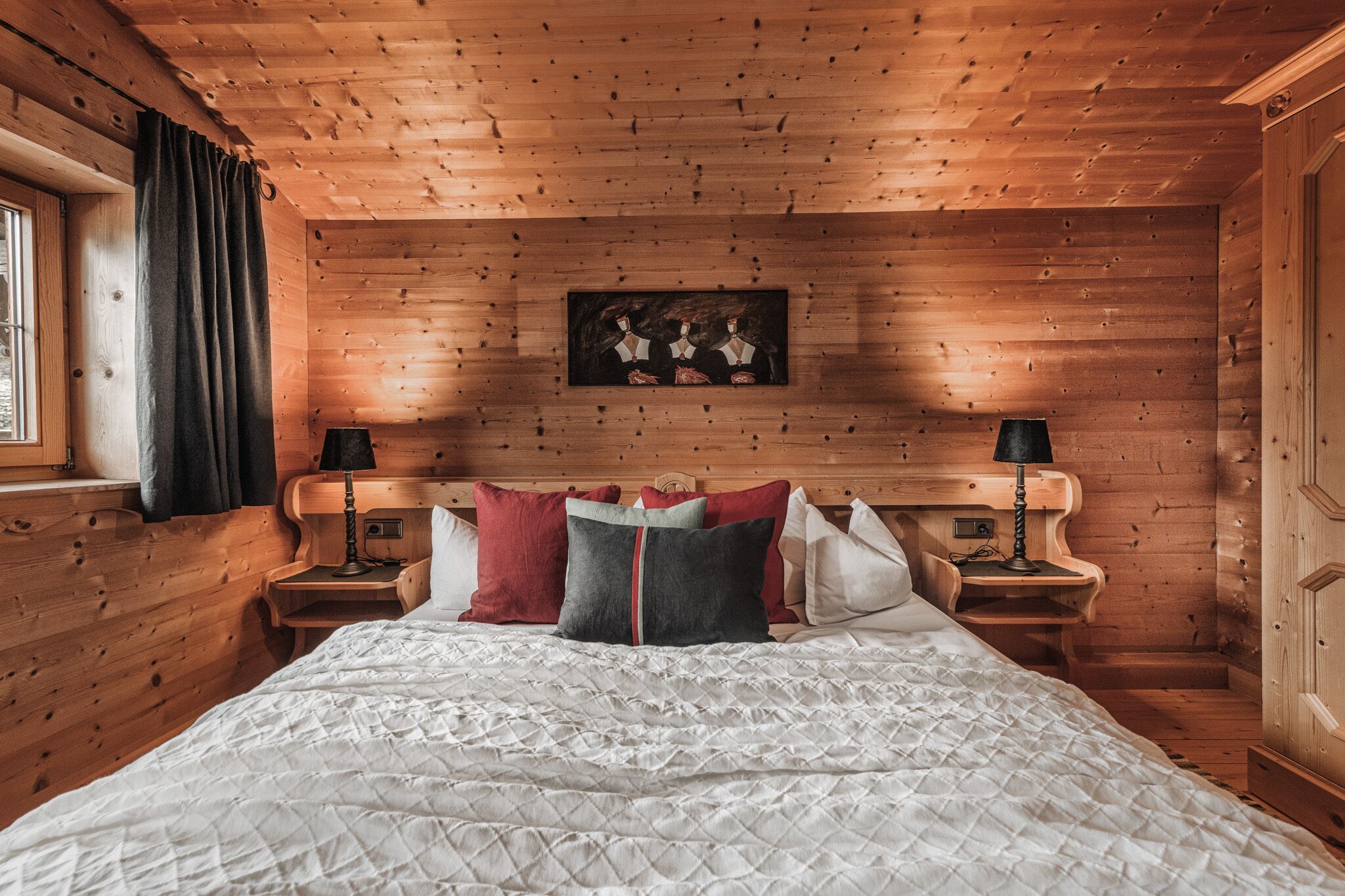 Un dormitorio de cabaña de madera con una cama grande, dos mesitas de noche y un cuadro enmarcado en la pared.
