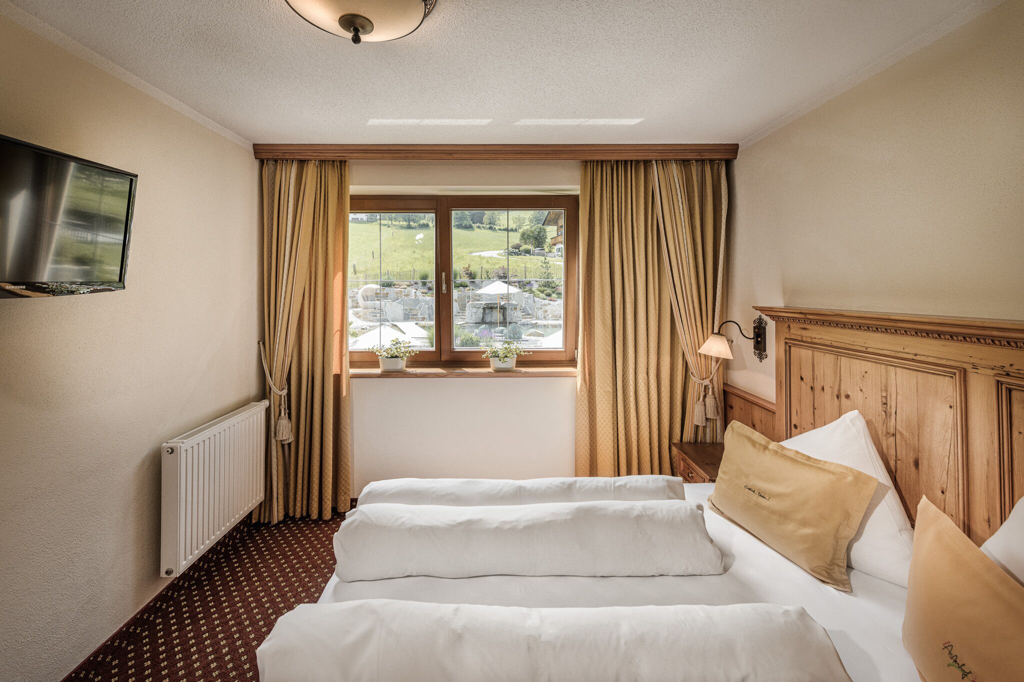 Ein Hotelzimmer mit zwei Betten, einem Fernseher, einem Fenster mit Vorhängen und Blick nach draußen.