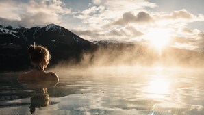 Iemand in een warmwaterbron, met bergen op de achtergrond.