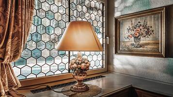 A room with a hexagonal window, a lamp on a table, and a framed painting on the wall.