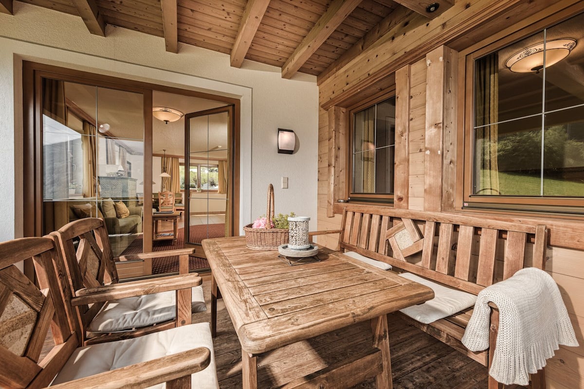 Un coin repas en bois avec une table et des bancs, un luminaire fixé au mur et une grande fenêtre donnant sur un paysage verdoyant.