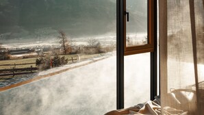 Een kamer met een groot raam met uitzicht op een bergachtig landschap en een rivier.