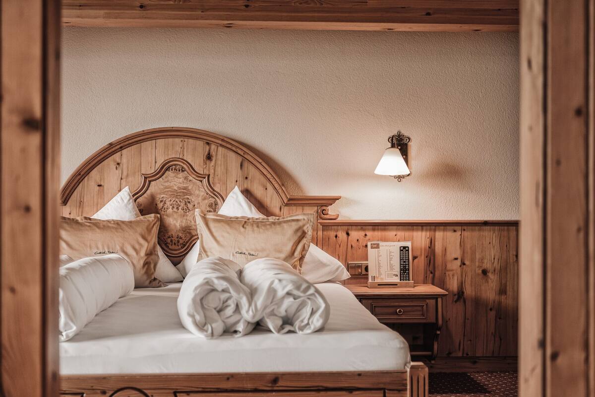 Un lit à cadre en bois, avec du linge de lit blanc et plusieurs oreillers, une table de chevet avec une lampe et un panneau mural en bois.